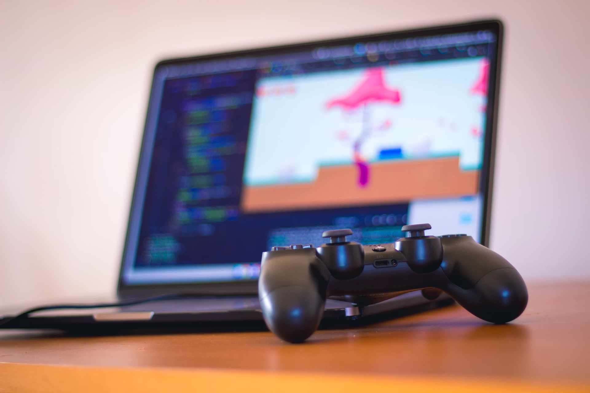 A laptop and game controller on a wooden desk representing indie game development and early access games in progress