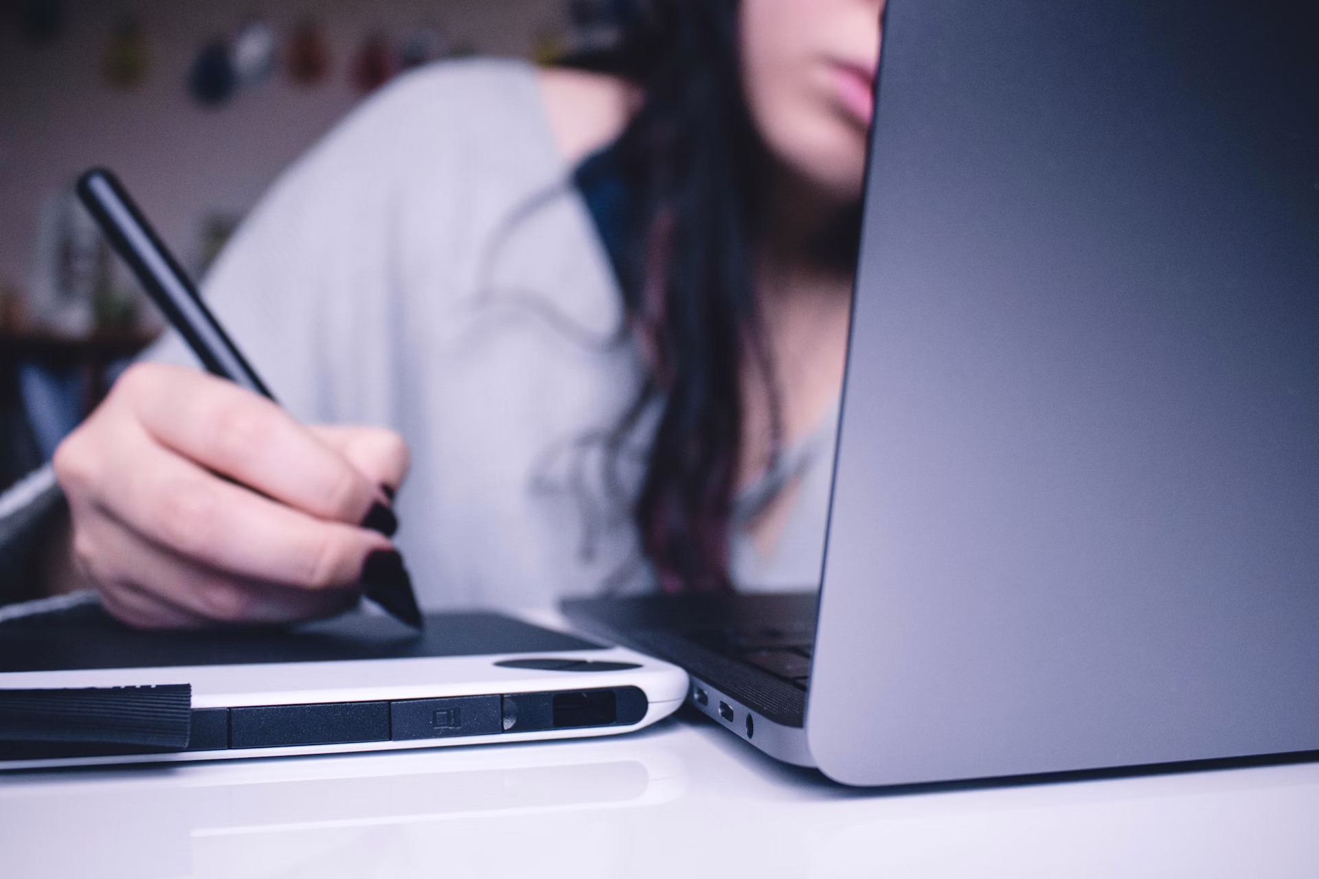 An artist drawing a character design on a digital tablet while seated at a laptop, illustrating the art-creation stage of a VTuber model commission