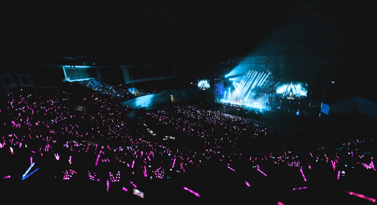 Massive concert audience holding colorful glow sticks and pen lights, representing Japanese idol fan culture and oshikatsu live event spending